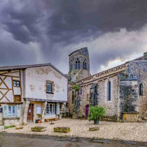 Photographie de l'église Saint-Jean-Baptiste avec la maison à colombages, en couleurs pastel, à Charroux, village de l'Allier,