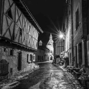 Photographie de la rue de l'horloge et de la porte-beffroi de l'horloge en noir et blanc la nuit à Charroux, village de l'Allier.