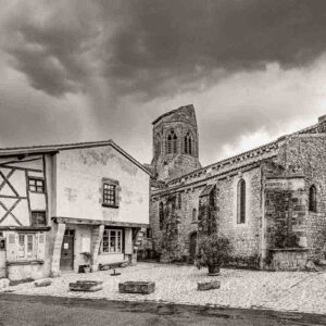 Photographie de l'église Saint-Jean-Baptiste et de la maison à colombage à Charroux, Allier, en version noir et blanc.