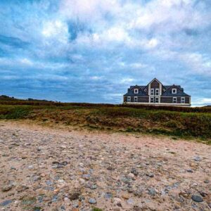 Photographie des galets de la baie et au fond l'hôtel de la Baie des Trépassés. Finistère, Bretagne. des Trépassés sous un ciel bleu gris.