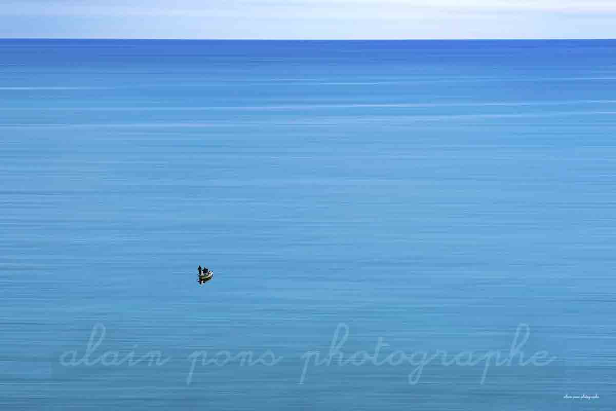 photographie de deux pêcheurs dans une barque sur une mer bleue. alain pons photographe®