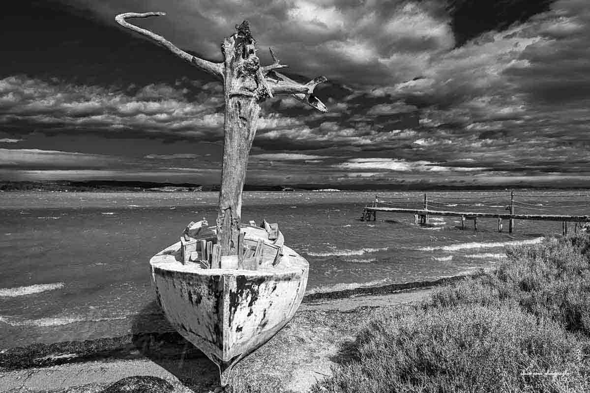 Photographie d'un bateau, un canot avec un mât en tronc d'arbre au bord d'un étang dans les Corbières. Ici présenté en simulation de décoration dans un salon. Version noir et blanc.