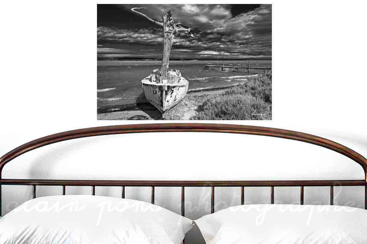Photographie d'un bateau, un canot avec un mât en tronc d'arbre au bord d'un étang dans les Corbières. Ici présenté en simulation de décoration dans une chambre. Version noir et blanc.