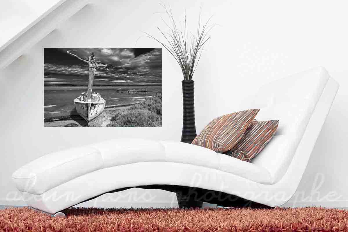 Photographie d'un bateau, un canot avec un mât en tronc d'arbre au bord d'un étang dans les Corbières. Ici présenté en simulation de décoration dans un salon. Version noir et blanc.
