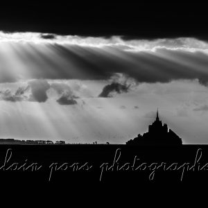 Photographie en noir et blanc du Mont-Saint-Michel sous des rayons lumineux,