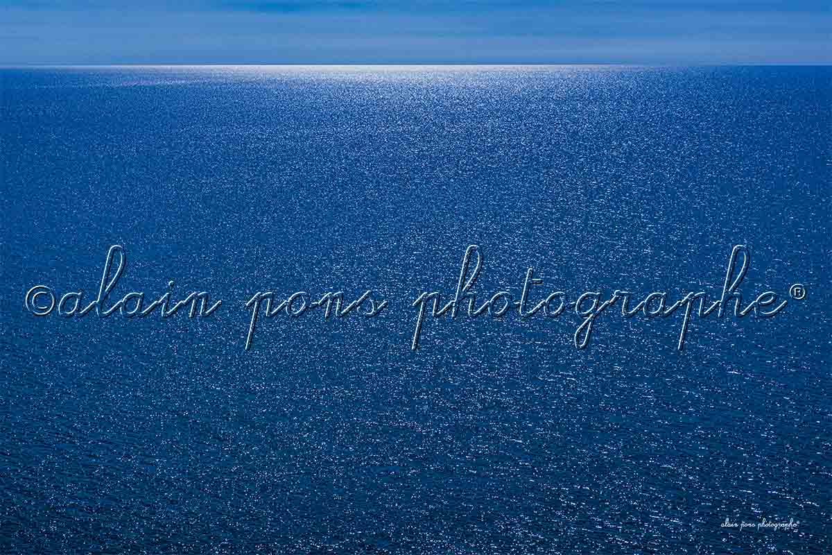 photographie Le grand bleu de la belle Méditerranée. Une mer entièrement bleue avec au fond de la mer à l'horizon un rayon de lumière blanche.